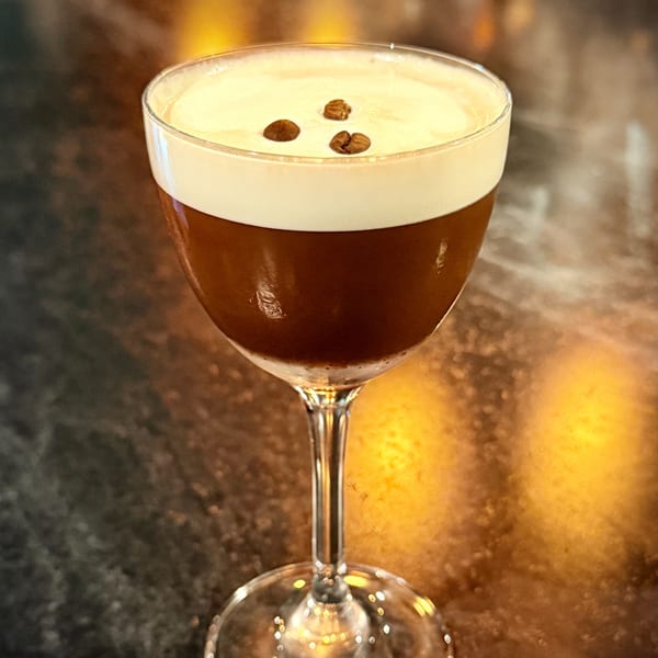 Espresso martini in a coupe glass, topped with creamy foam and three coffee beans.