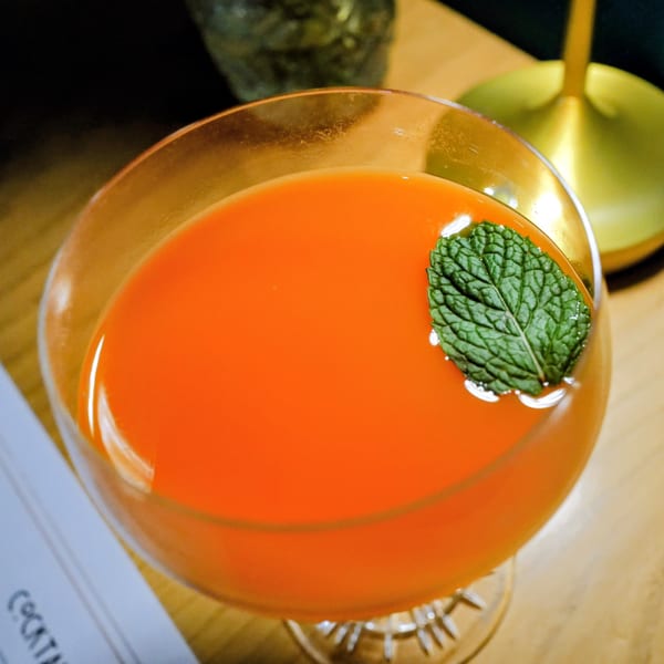 Vibrant orange cocktail in a stemmed glass, garnished with a fresh mint leaf.